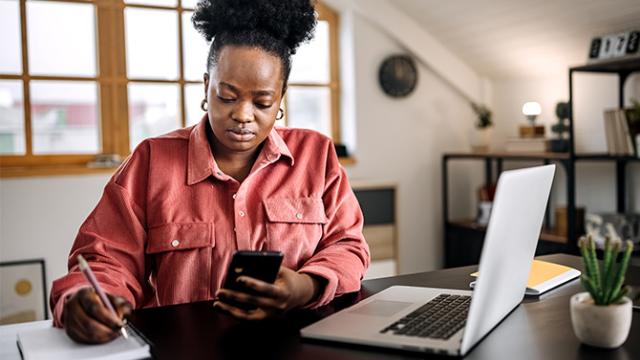 female executive analyzing her travel management company with her laptop open and cell phone in hand