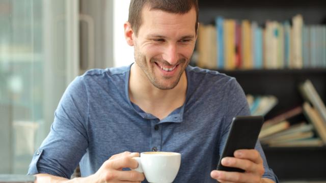 Happy adult man checking smart phone holding a cup knowing that breakfast and WiFi is included in his hotel rate