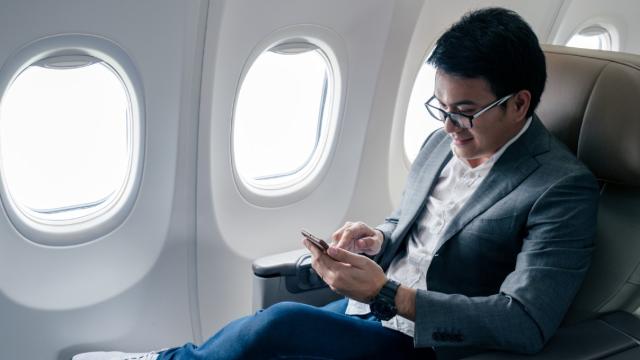 Asian male traveller on his phone on an airplane