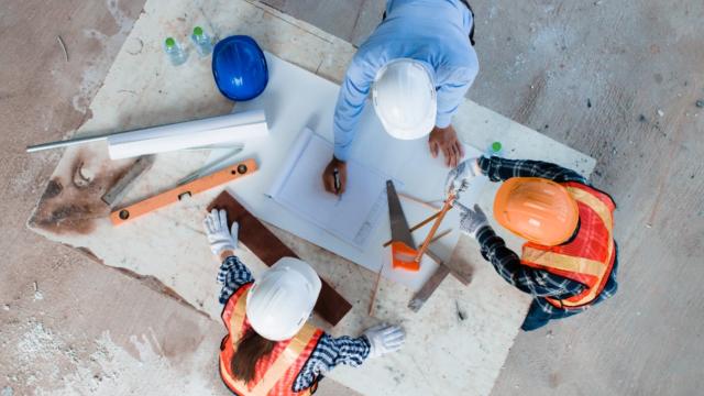 Team of young man and woman engineer and architects working, meeting, discussing,designing, planing, measuring layout of building blueprints in construction site floor at factory