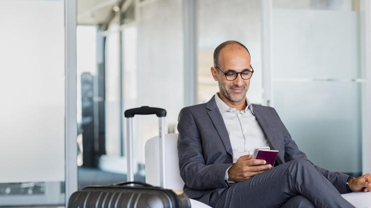 Mature businessman using mobile phone at the airport in the waiting room. Business man typing on smartphone in lounge area.