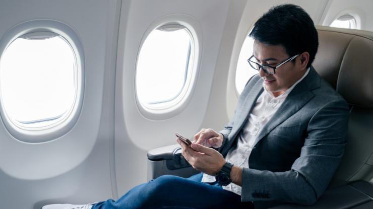 Asian male traveller on his phone on an airplane