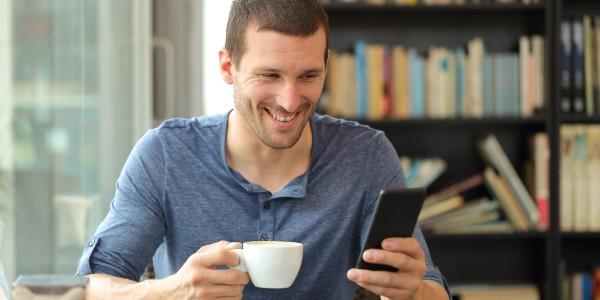 Happy adult man checking smart phone holding a cup knowing that breakfast and WiFi is included in his hotel rate