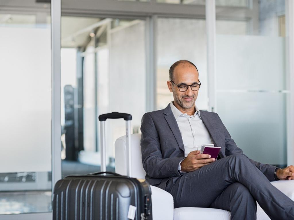 Mature businessman using mobile phone at the airport in the waiting room. Business man typing on smartphone in lounge area.