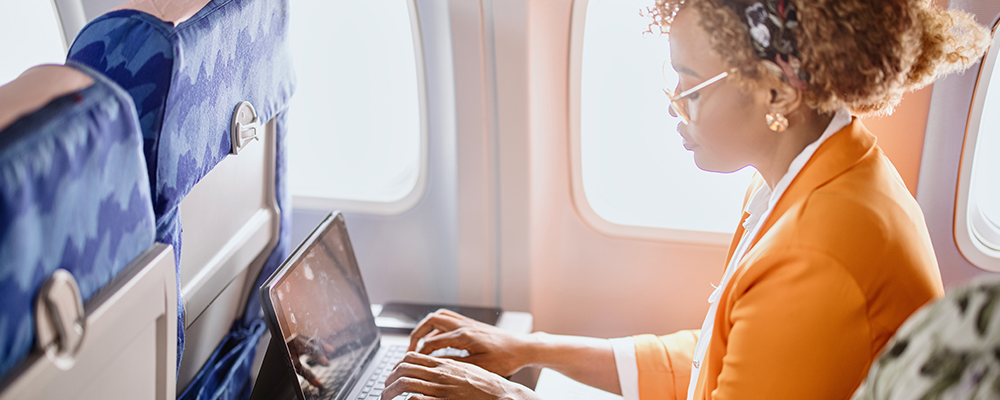 A young woman working on a laptop while seated in an airplane seat representing meaningful ways to engage with Youth Day. 