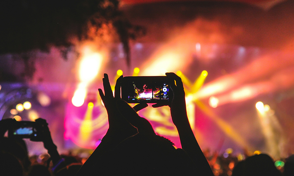 A concert scene with bright lights, as a person records the performance on a smartphone.