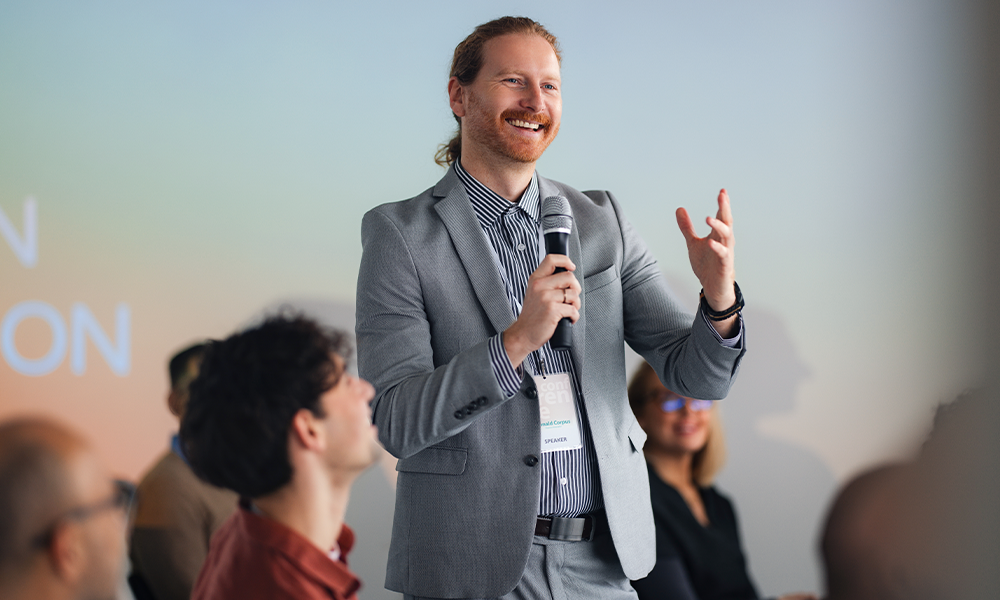 A man in a suit speaks into a microphone, engaged in conversation at a seminar.