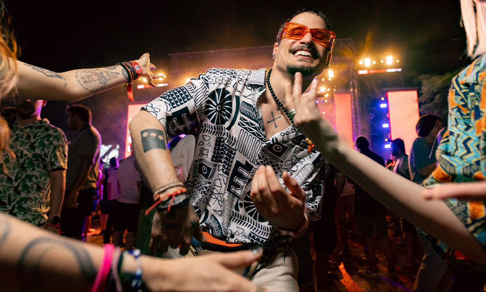 A man dances joyfully at a vibrant party, surrounded by colorful lights and energized people.