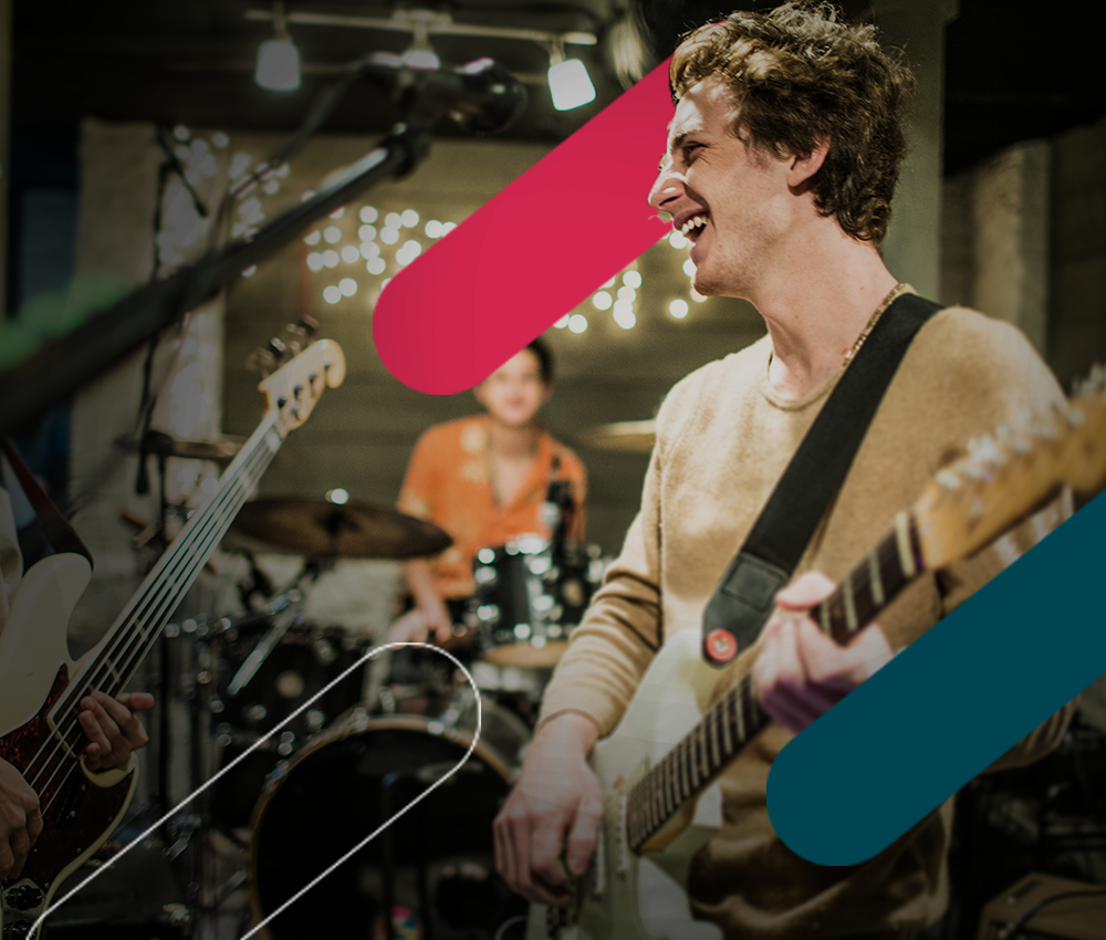 Two guitarists and a drummer playing in a warmly lit rehearsal space