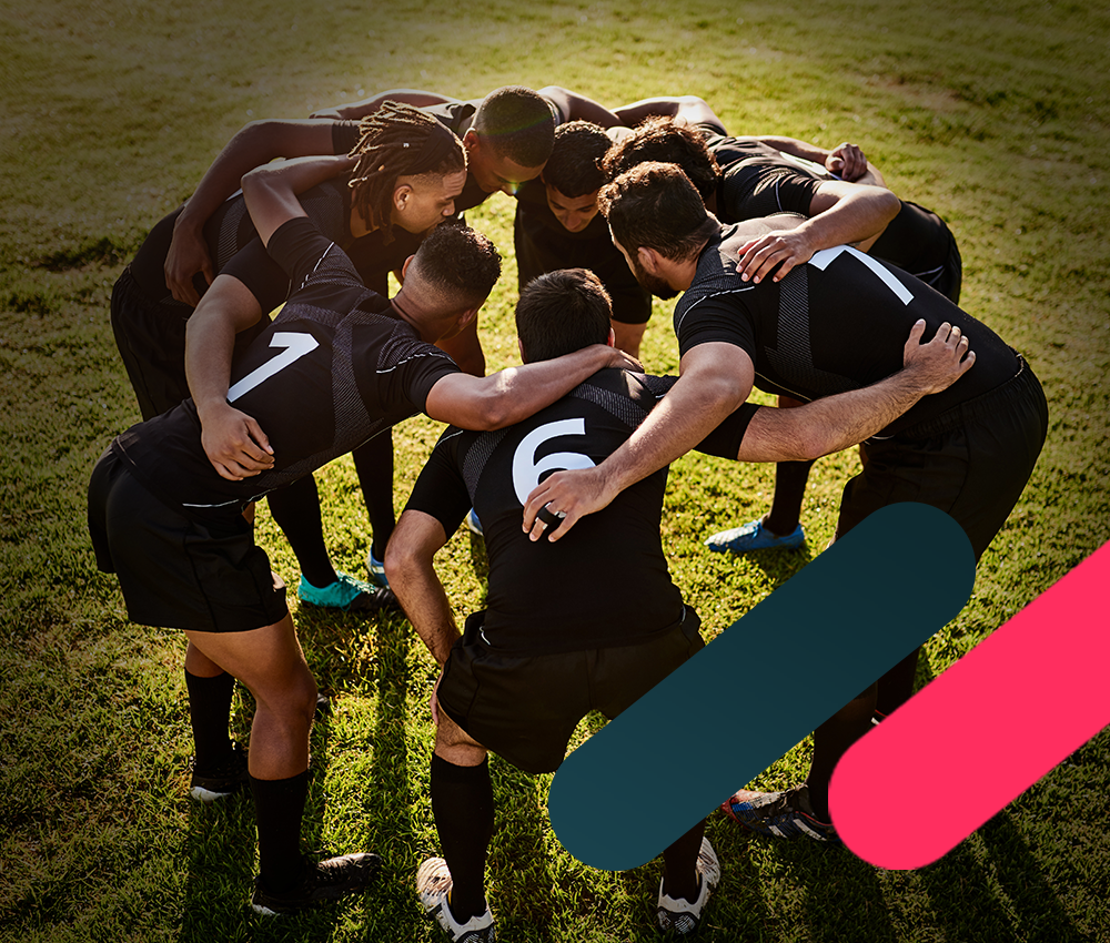 Soccer team in black jerseys huddled together on sunlit grass field