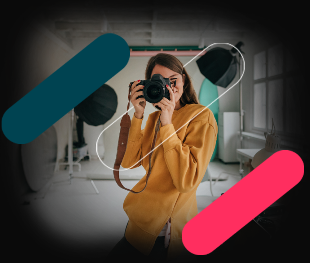 Woman in yellow sweater photographing in studio with teal and pink graphic bars
