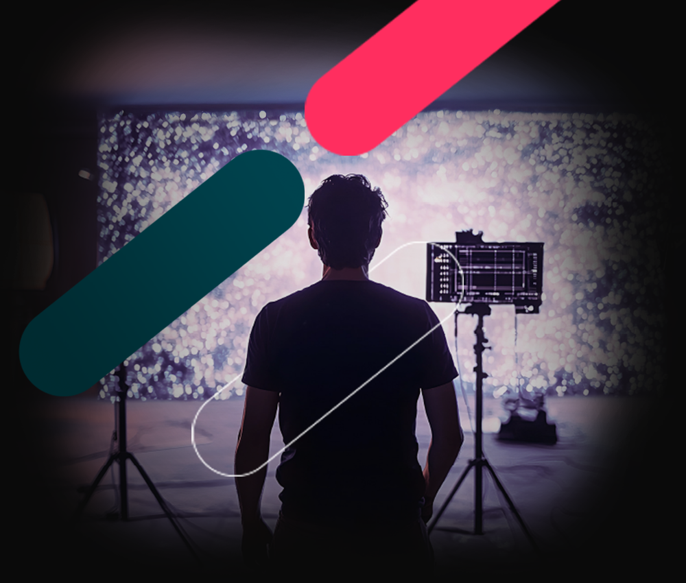 Silhouette of a person facing a bright screen in a studio with lights and camera gear.