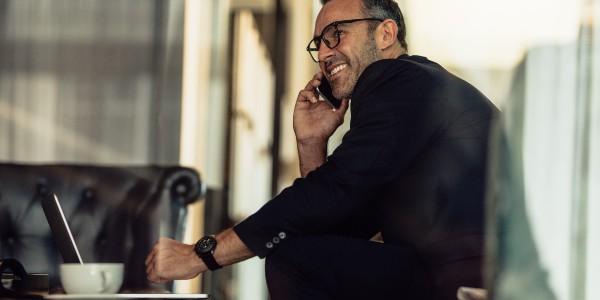 Man talking on the phone with a cup of coffee and his laptop happy that we've got his trip sorted