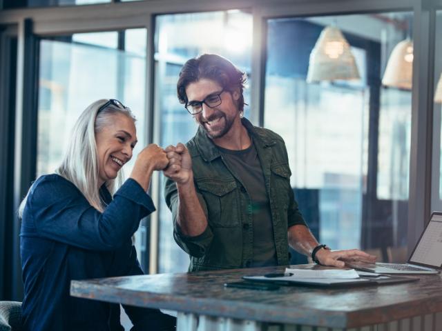 Young businessman and senior businesswoman making a fist bump at office. Business colleagues looking happy and excited after completion of project.