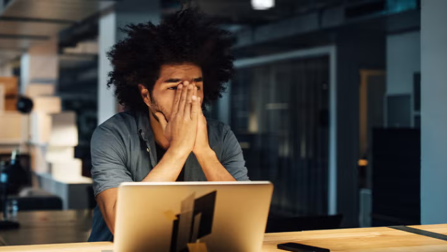 Man sitting in front of laptop with hands on face looking frustrated representing why DIY travel bookings are bad for business.