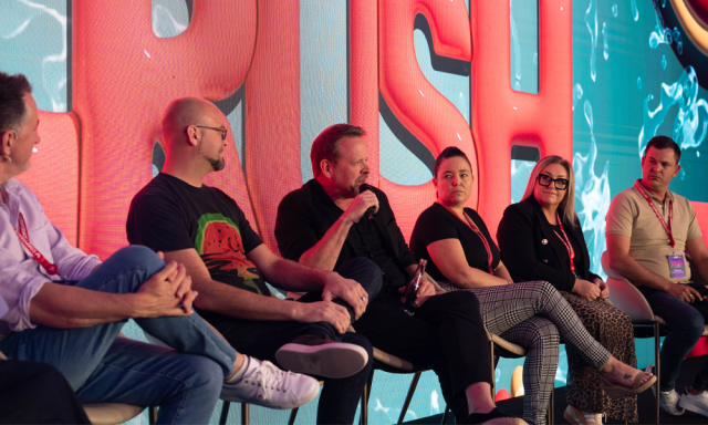 A panel discussion featuring five individuals seated, with a colorful backdrop.