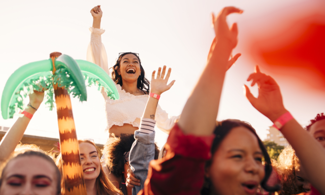 Joyful crowd at a festival with a girl celebrating atop a faux palm tree.